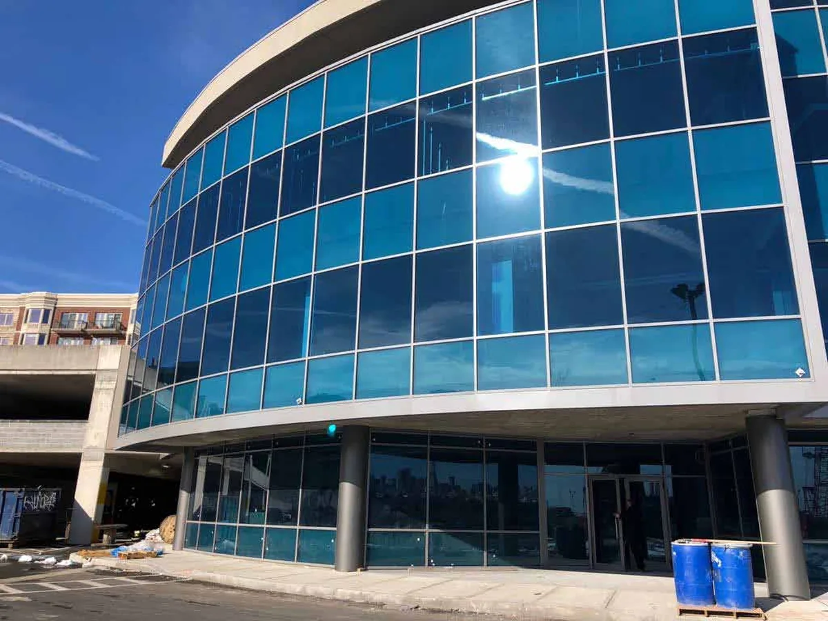Curved commercial building elevation clad in dark reflective glass carried on slim aluminum curtain wall mullions, photographed from street level in daylight.