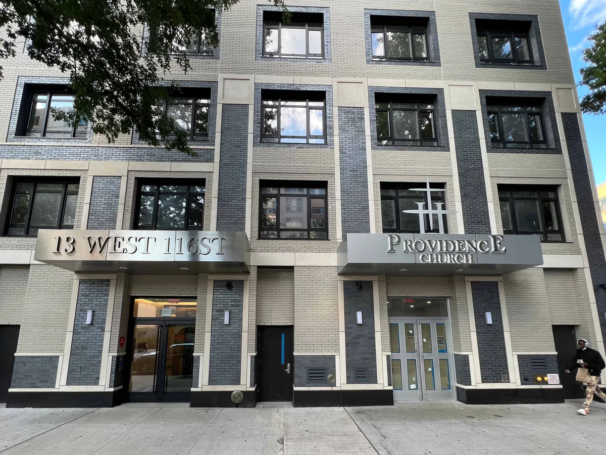 Masonry building frontage at ground level with dark aluminum storefront framing around glazed entrance doors and fixed display lights.