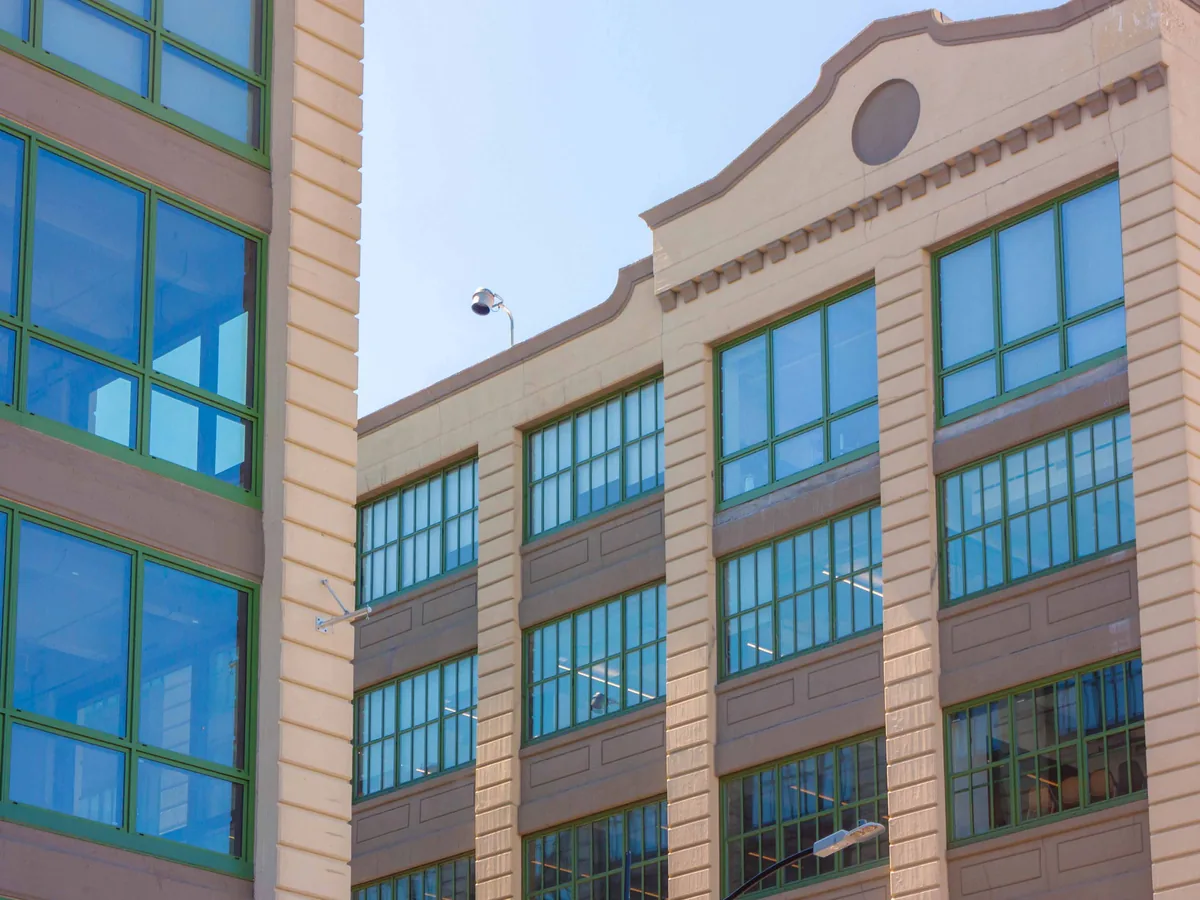Multi-storey brick facade with regular bays of large aluminum-framed windows in a dark finish, reflecting blue sky.