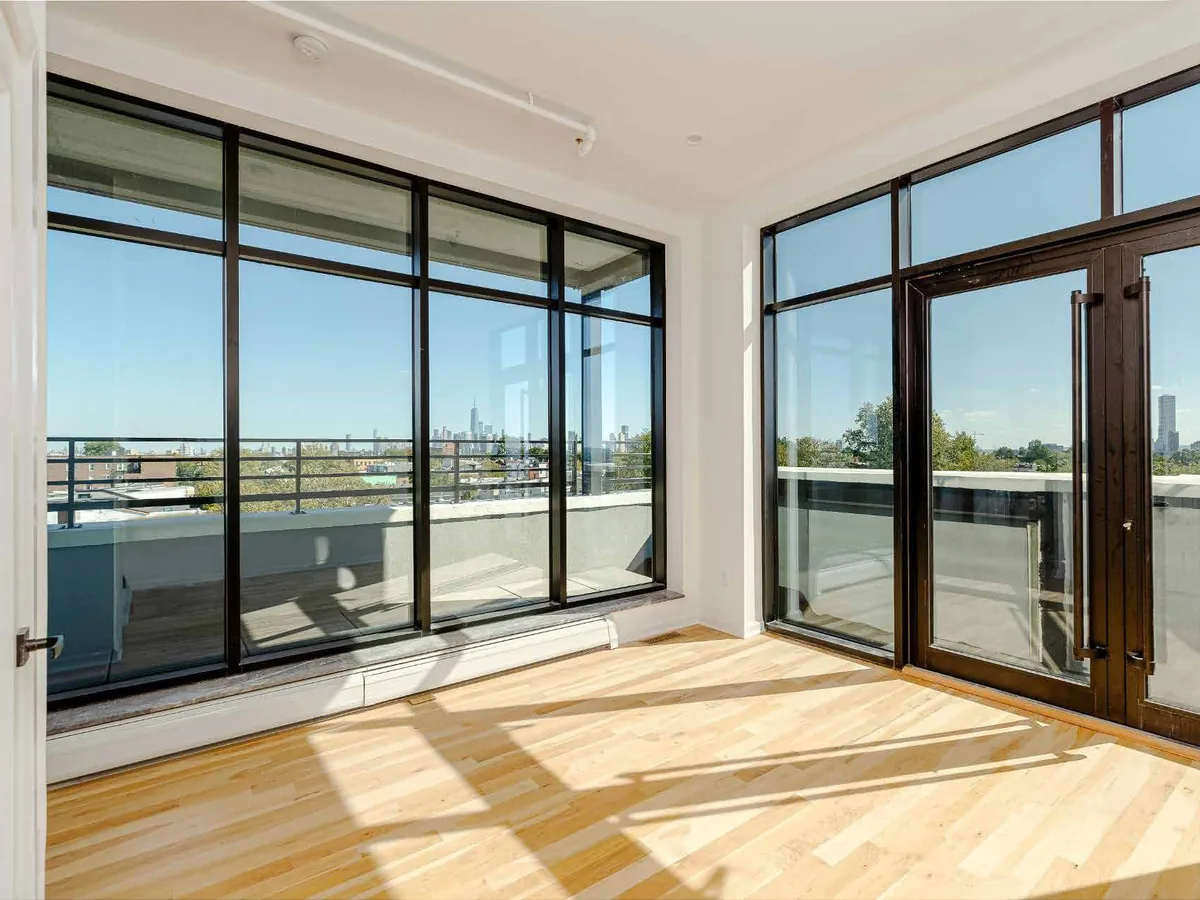 Empty interior room with pale timber flooring opening through wide aluminum-framed sliding glass doors onto a terrace with a distant skyline.