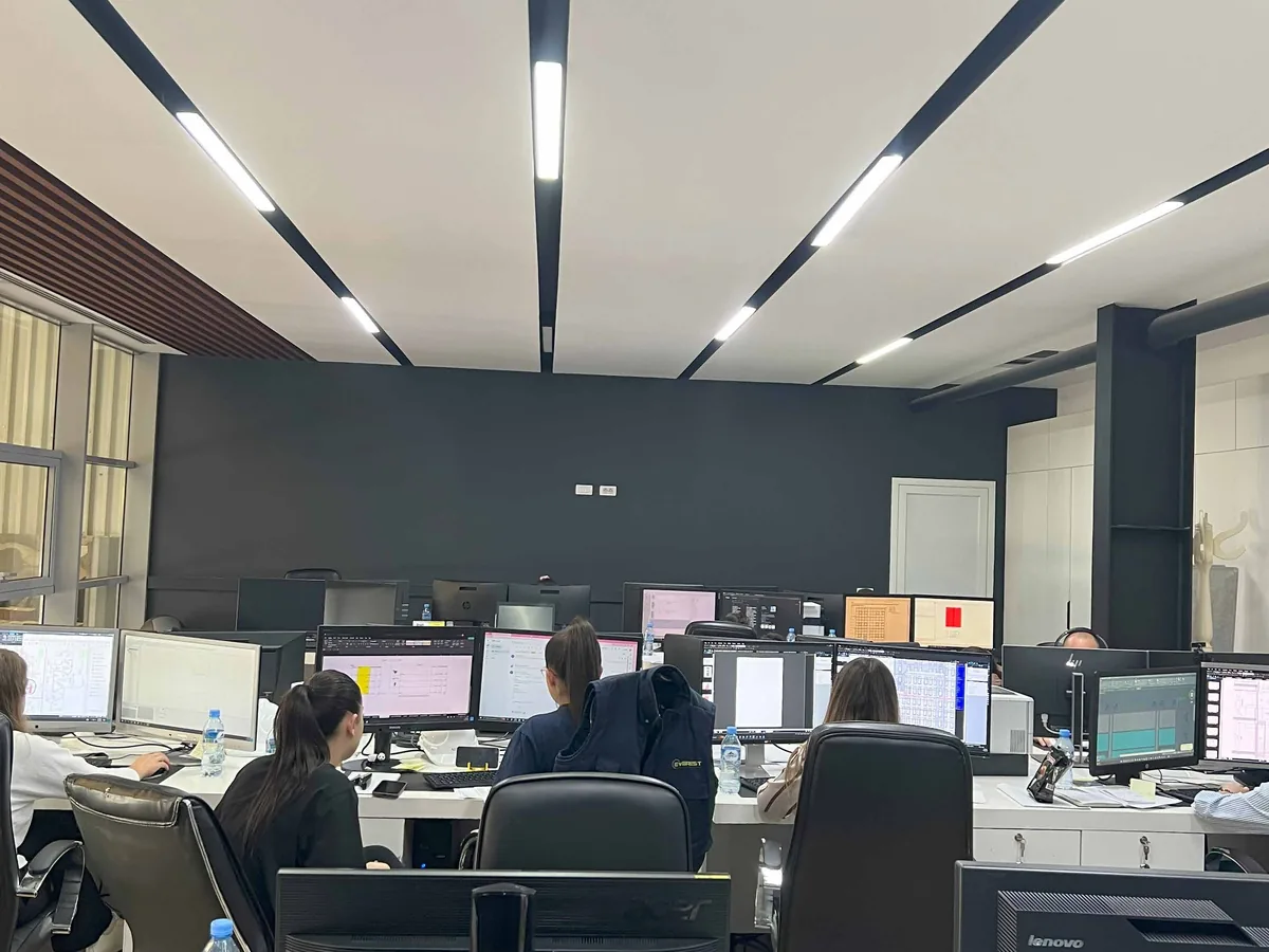Technical office with staff working at dual-monitor workstations under linear ceiling lighting.