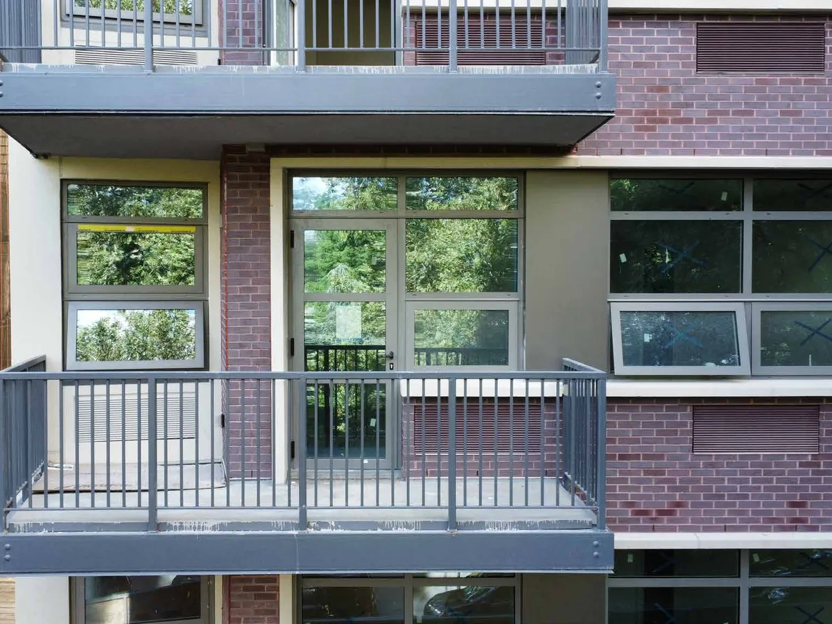 Close view of a brick residential elevation with inward-opening aluminum window sashes beside a balcony with a metal guard rail.