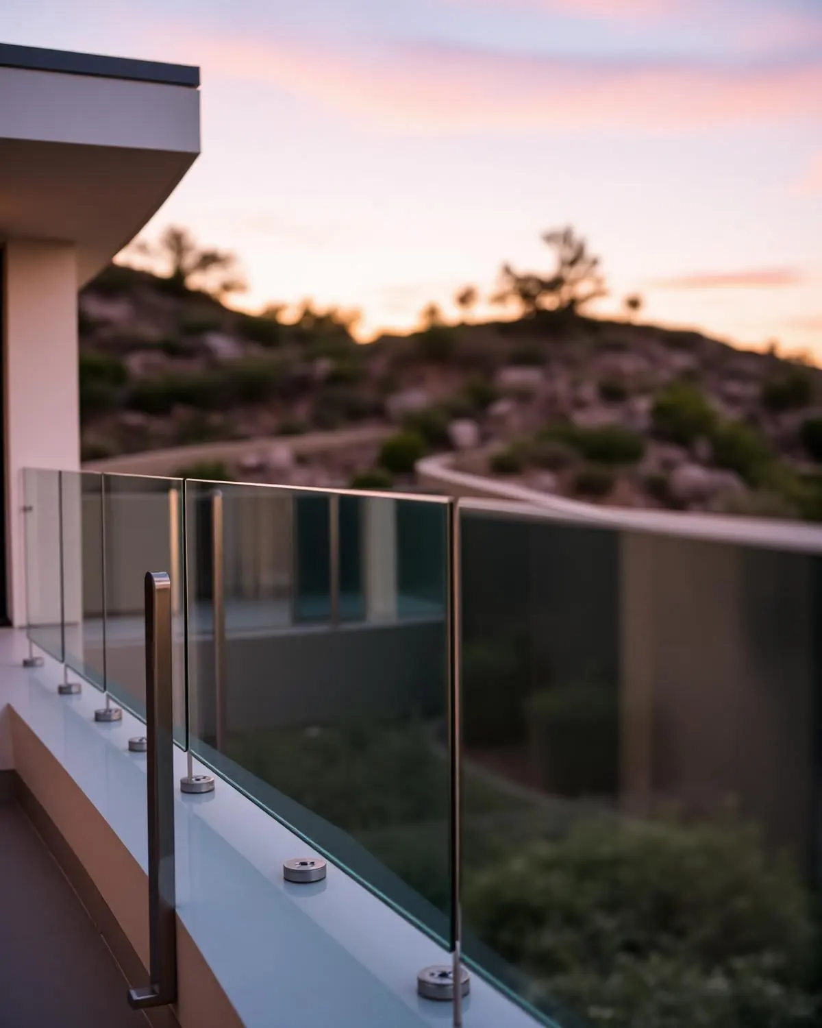 Frameless glass railing with stainless standoffs on a modern hillside home at sunset