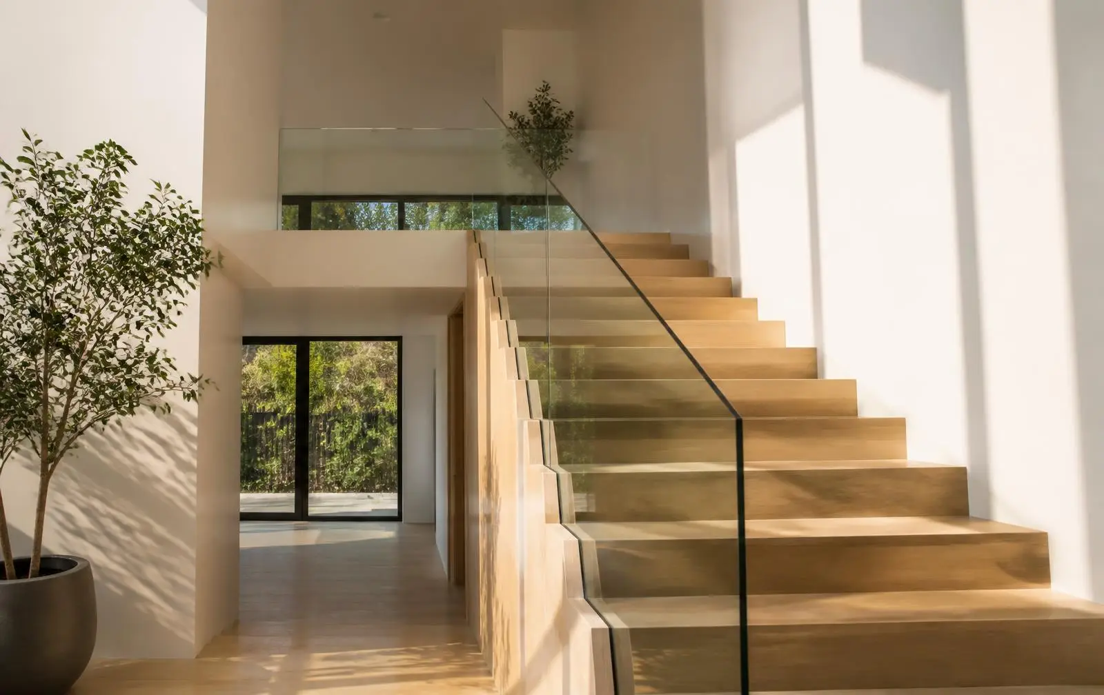 Design reference: a wide daylit interior where frameless glass panels divide a living area from a planted courtyard